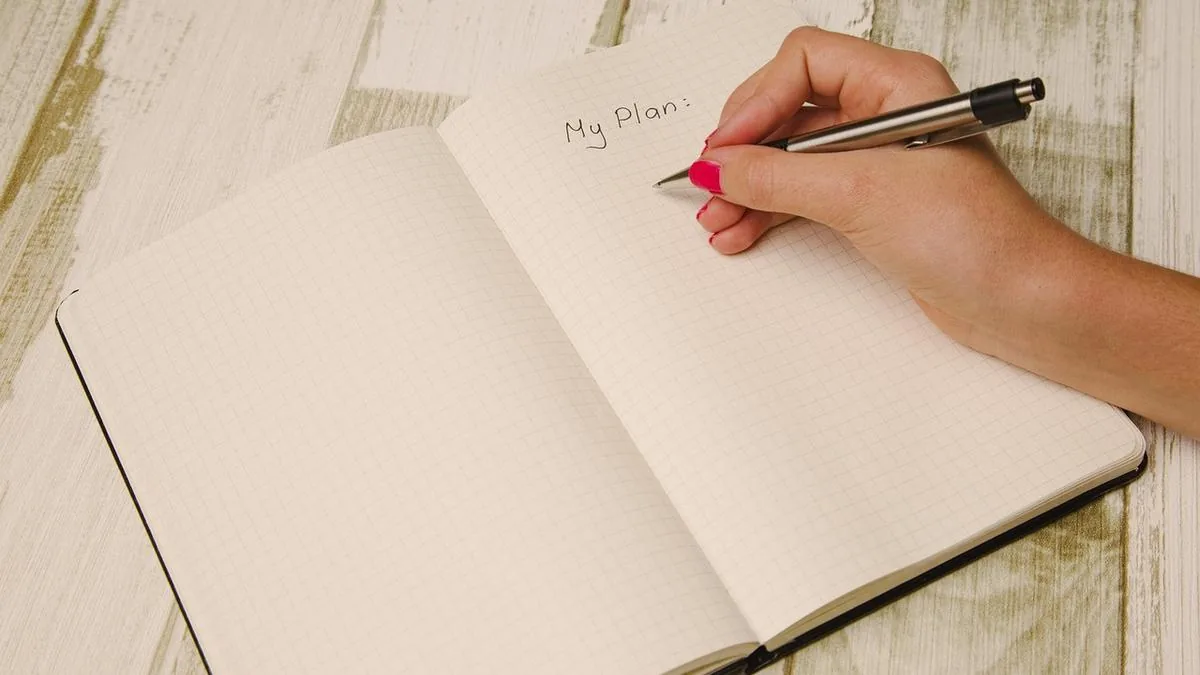 A woman's hand writing a plan in a notebook, tracking tasks and next steps